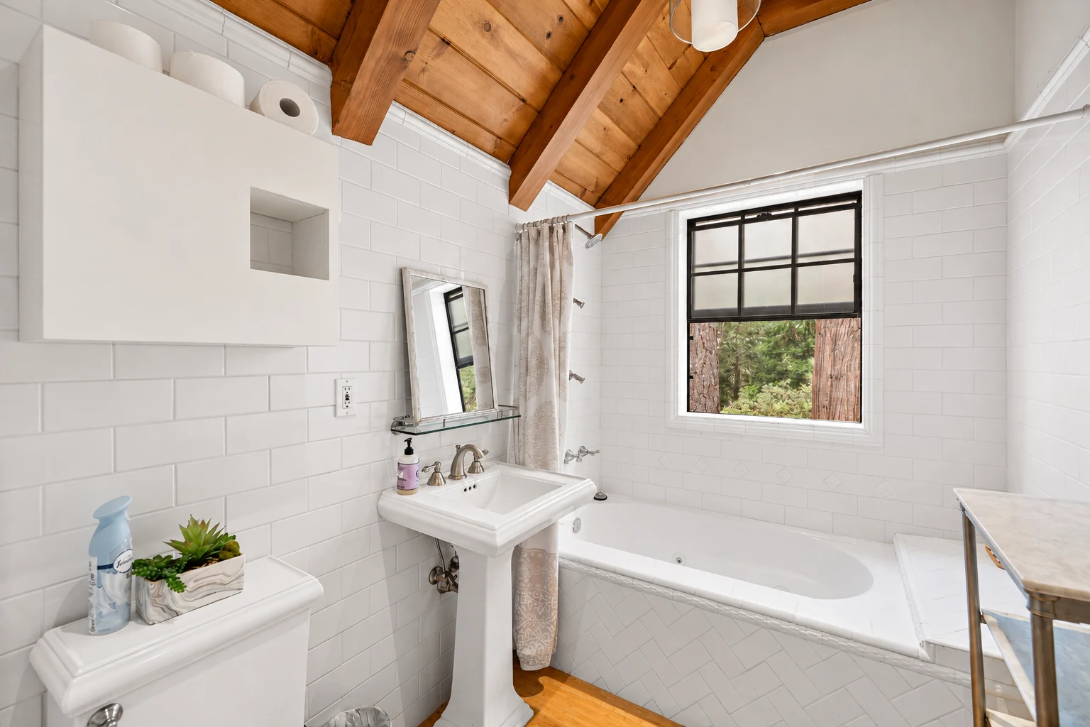 A bathroom with a tub beneath a window, white tile and a pedestal basin