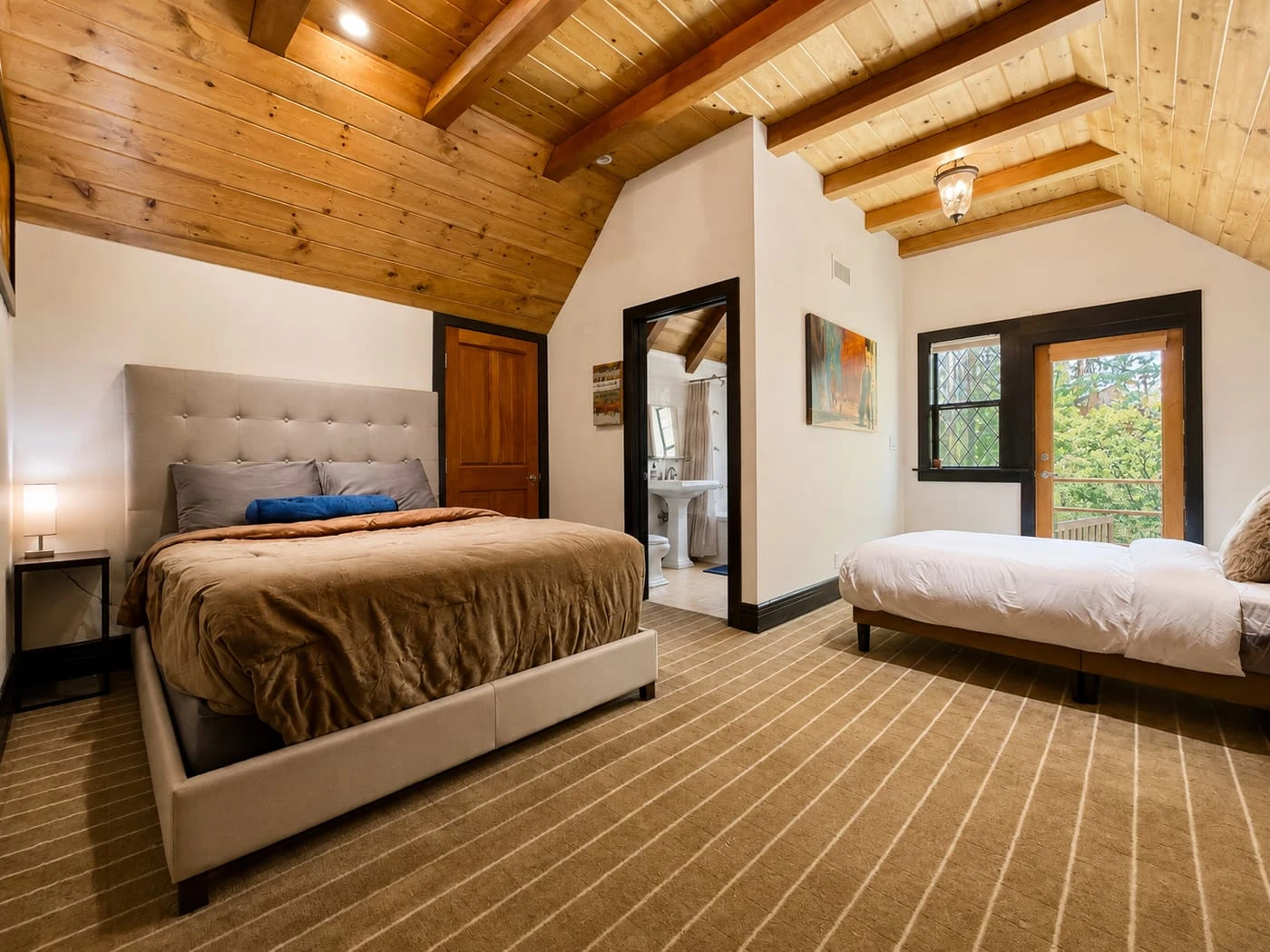 A bedroom with a vaulted wood ceiling, two beds and an ensuite bath