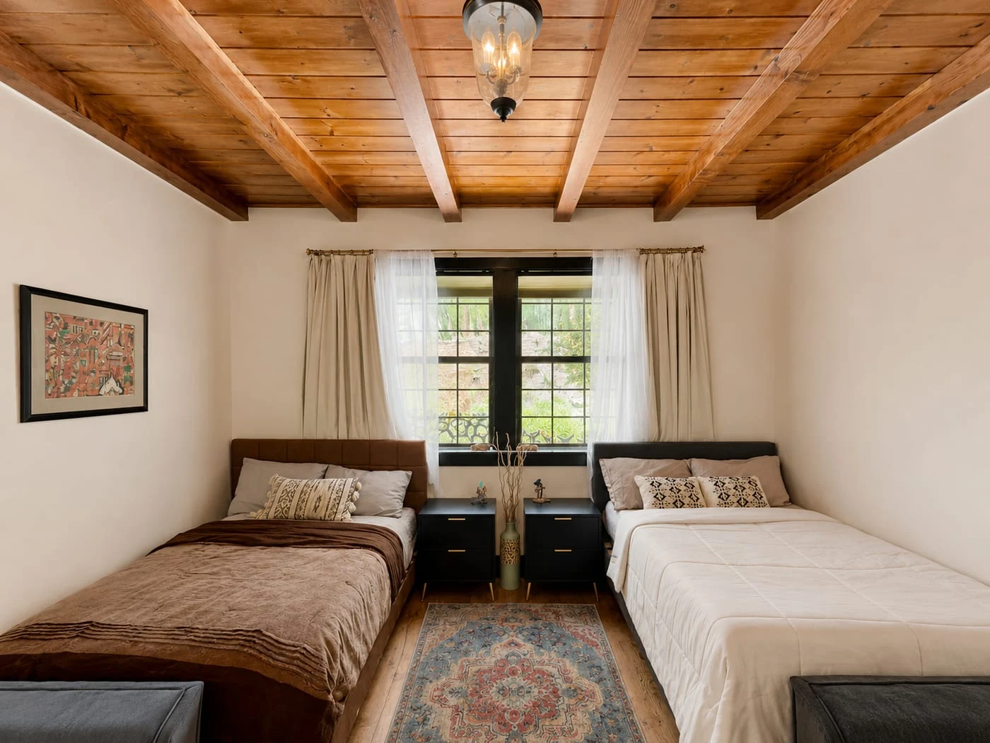 A bedroom with two beds under a wood-beam ceiling and a window to the trees