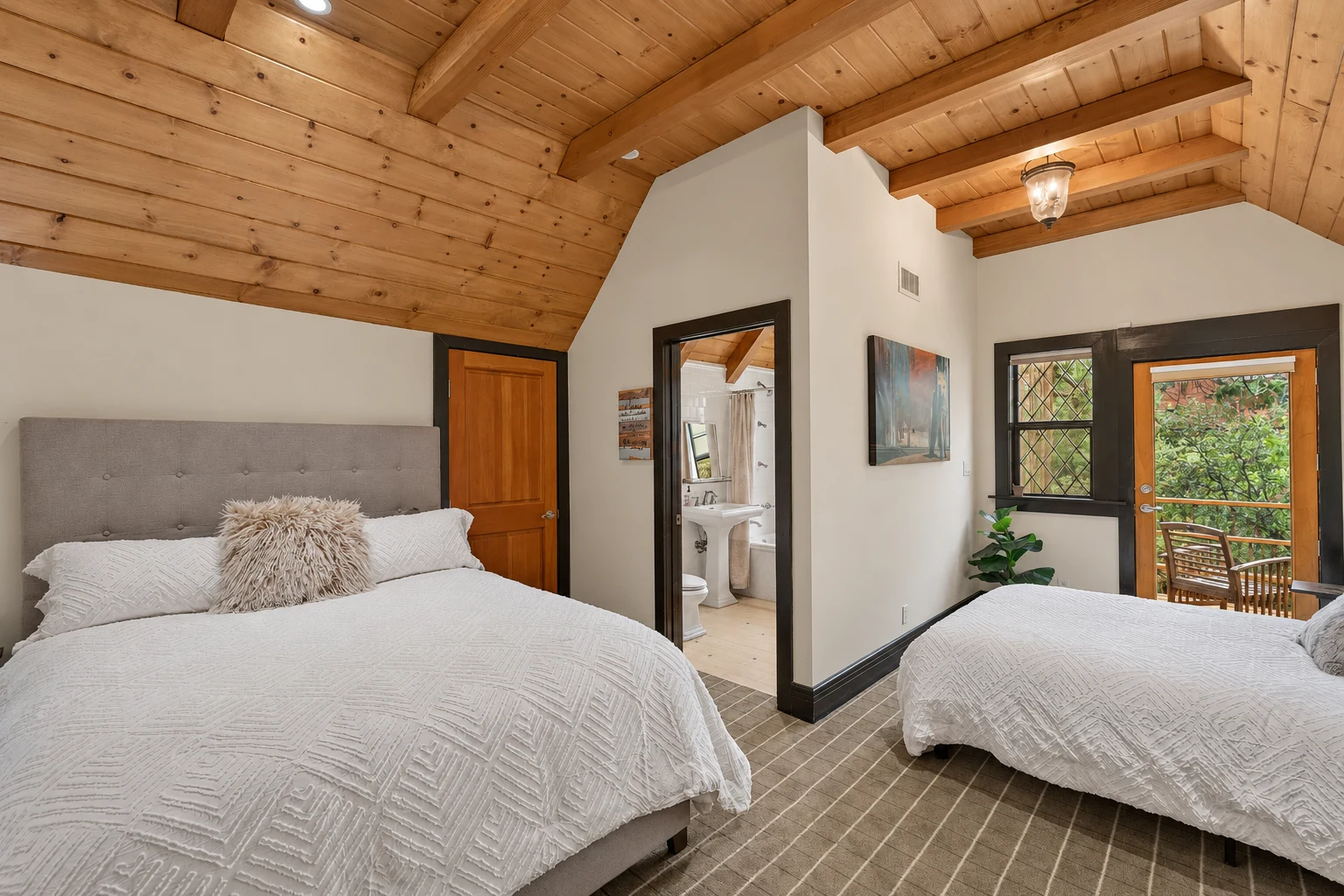 A bedroom with a vaulted wood ceiling, two beds and an ensuite bath
