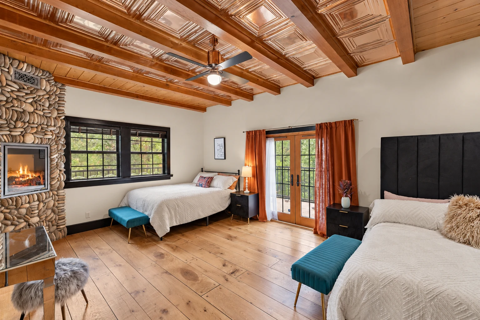 A bedroom with two beds, a river-stone fireplace and French doors under a coffered wood ceiling
