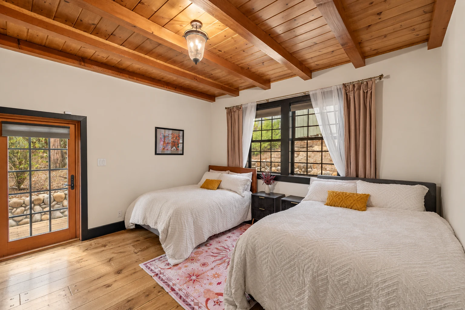 A bedroom with two beds under a wood-beam ceiling and a window to the trees