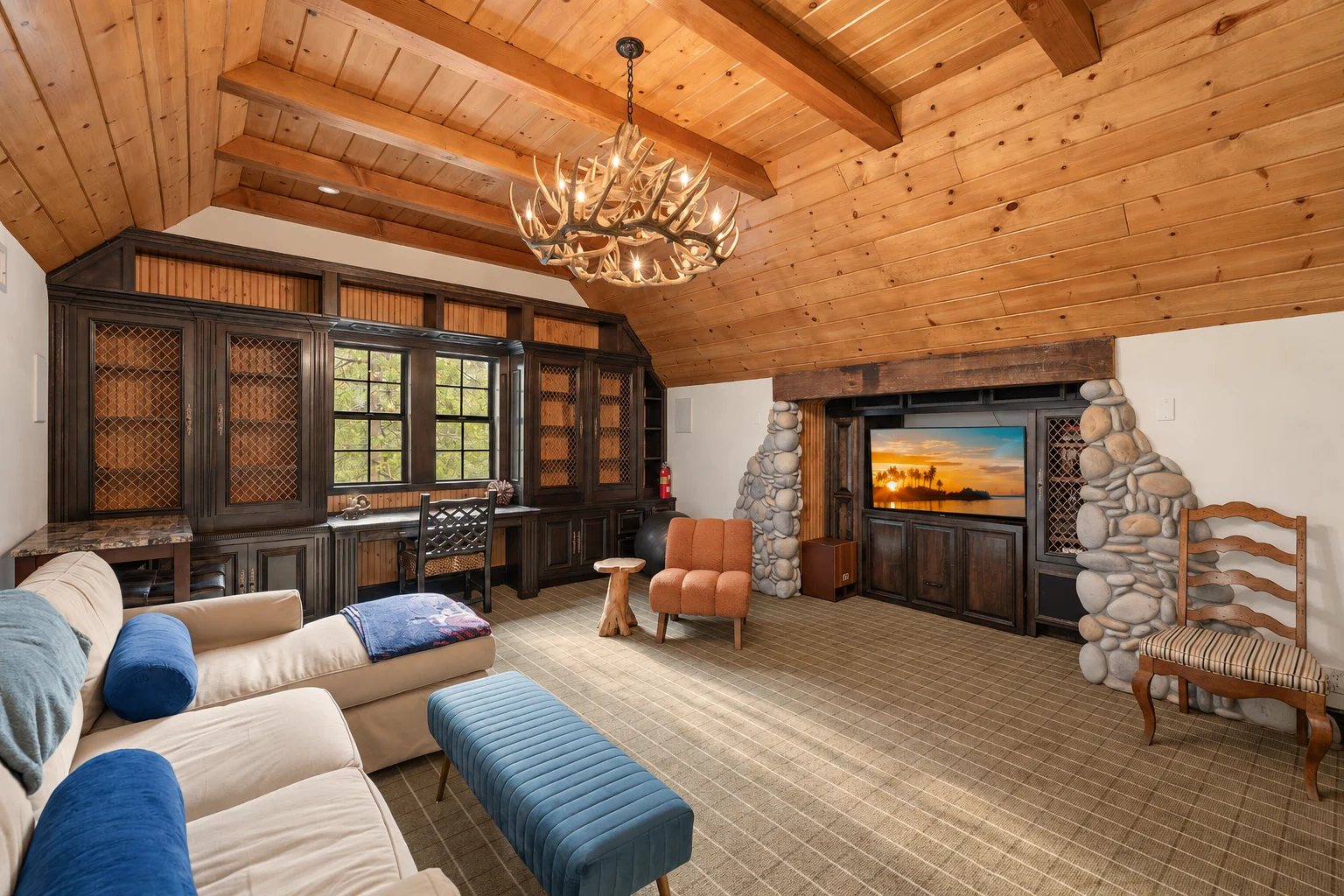 A common room under a beamed wood ceiling, with sofas, built-in desks and a river-stone wall