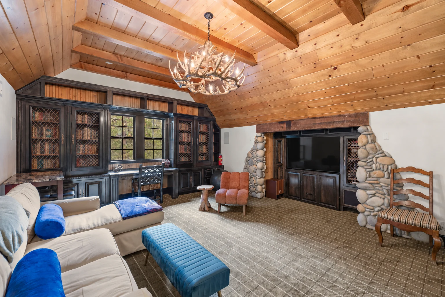 A common room under a beamed wood ceiling, with sofas, built-in desks and a river-stone wall