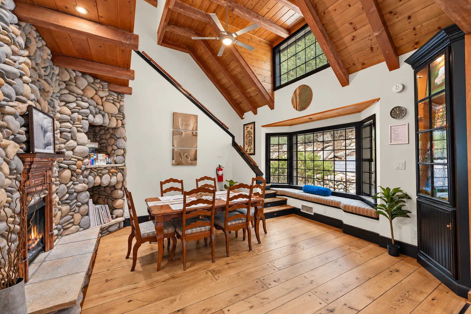The dining table beside the river-stone fireplace, with a cushioned window seat