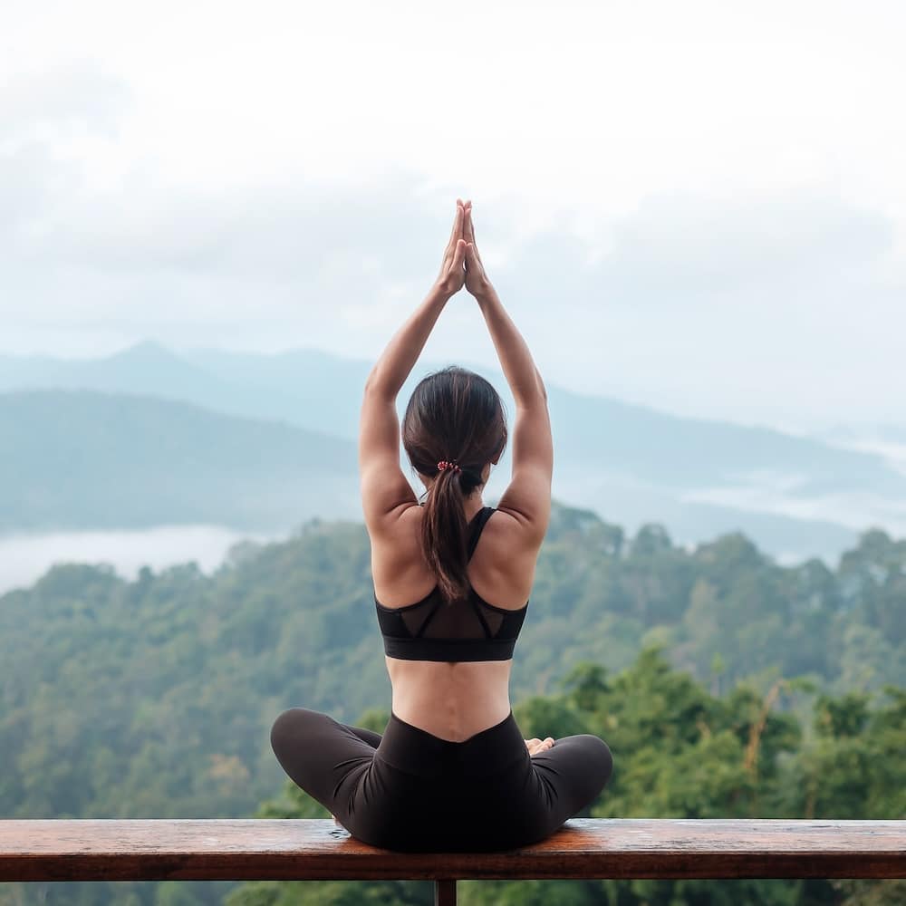 Young woman doing Yoga against mountain view.