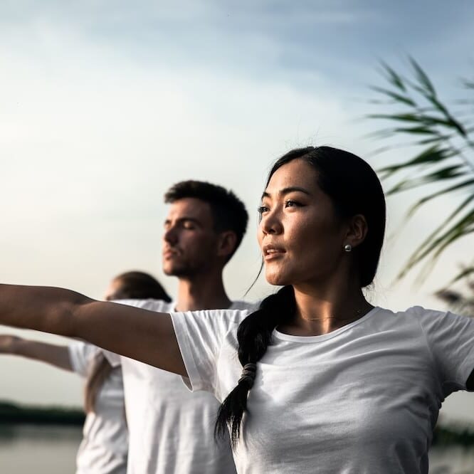 Group of people doing tai chi by the lake at sunset.