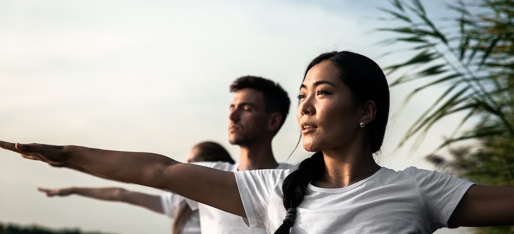 Group of people doing yoga exercises by the lake at sunset.