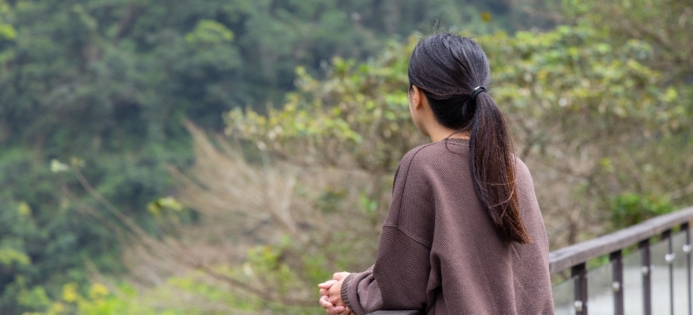 Woman looking out over tree line at a waterfall