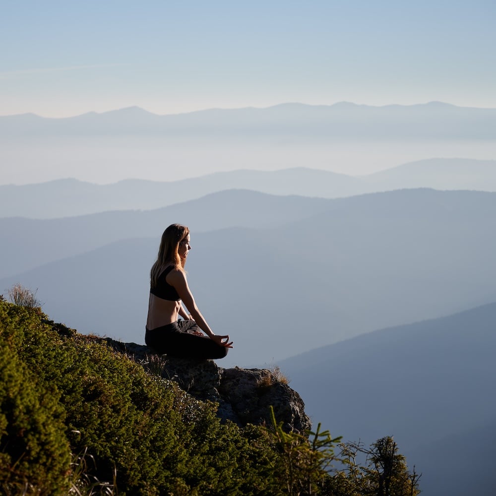 Side view of woman sitting in meditation in the mountains.