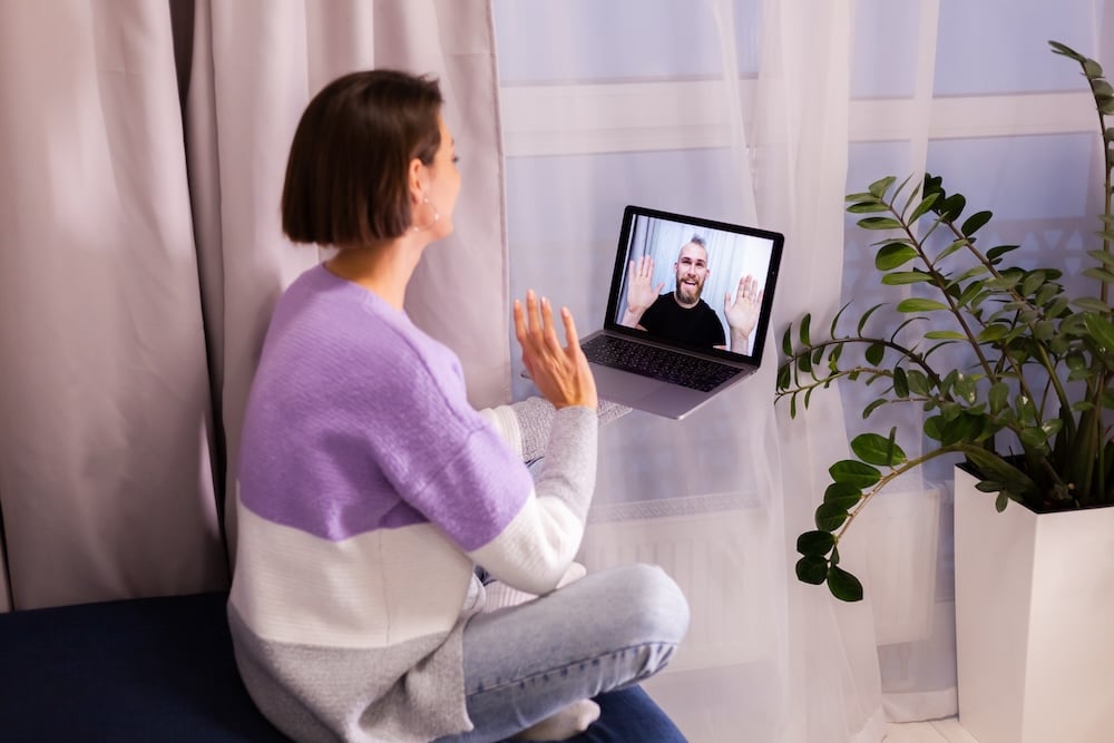 Woman sitting on her laptop talking to online therapist and waving hello