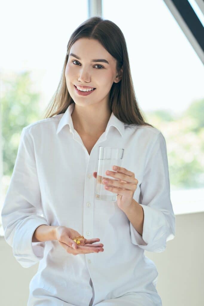 Young woman holding medications with a glass of water.