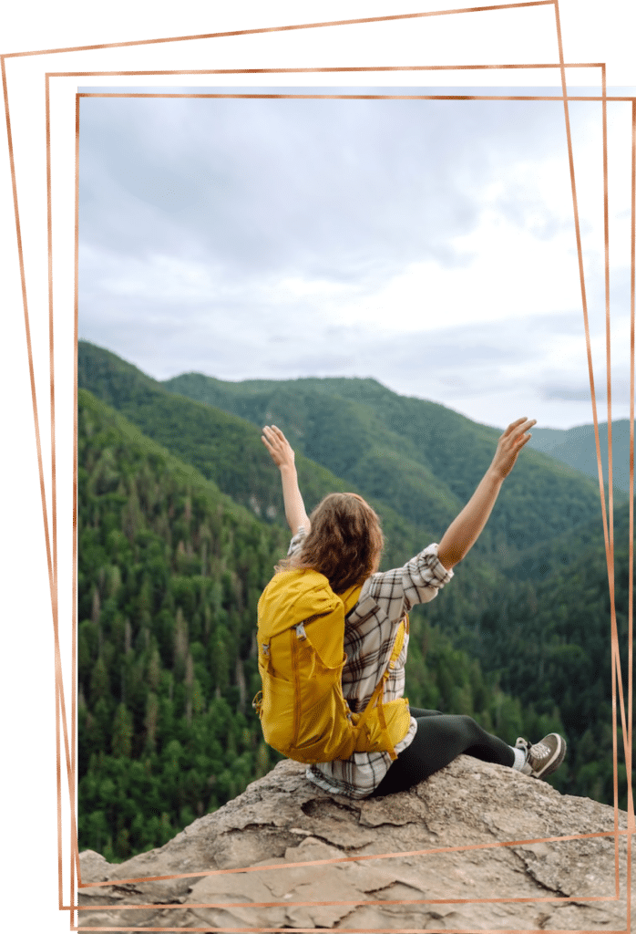 Young woman sitting on the edge of a cliff overlooking tall, towering pine trees in the mountains on a healing journey.