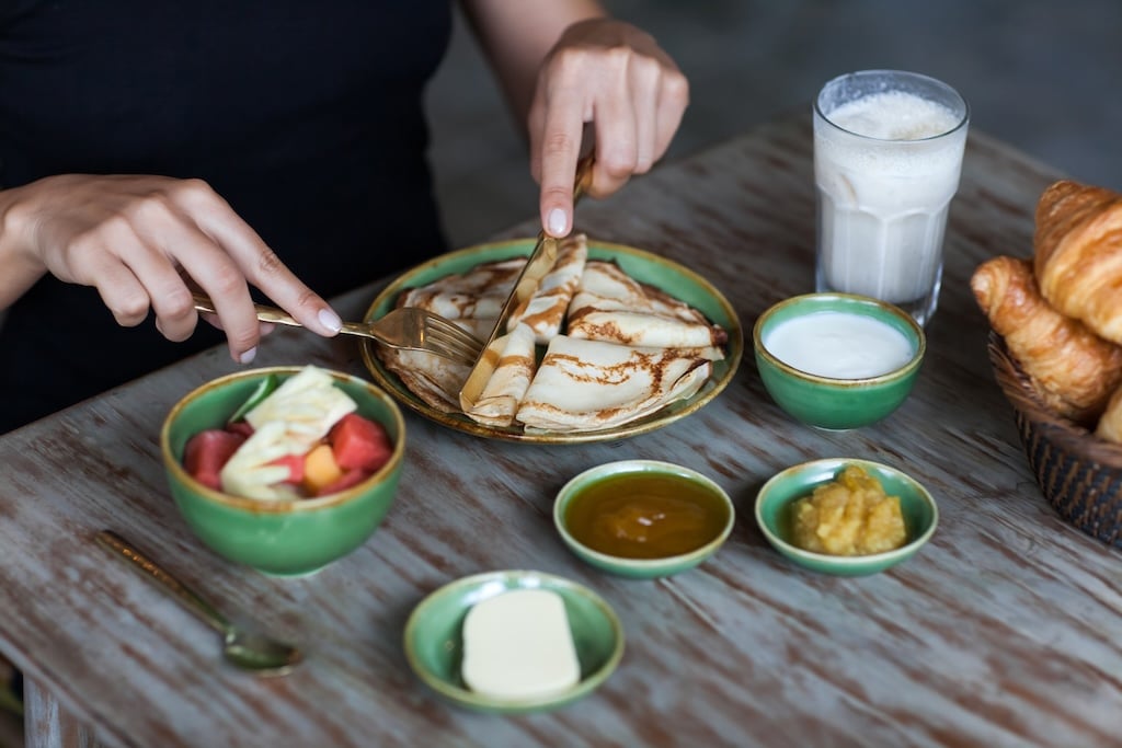 Young woman having breakfast and cut pankaces with golden fork and knife