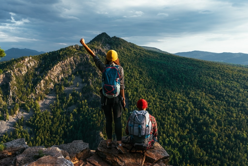 Traveling friends in hiking gear in the mountains at sunset with backpacks.