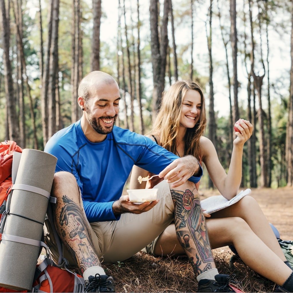 People sitting together while hiking, having a snack and laughing in the forest.