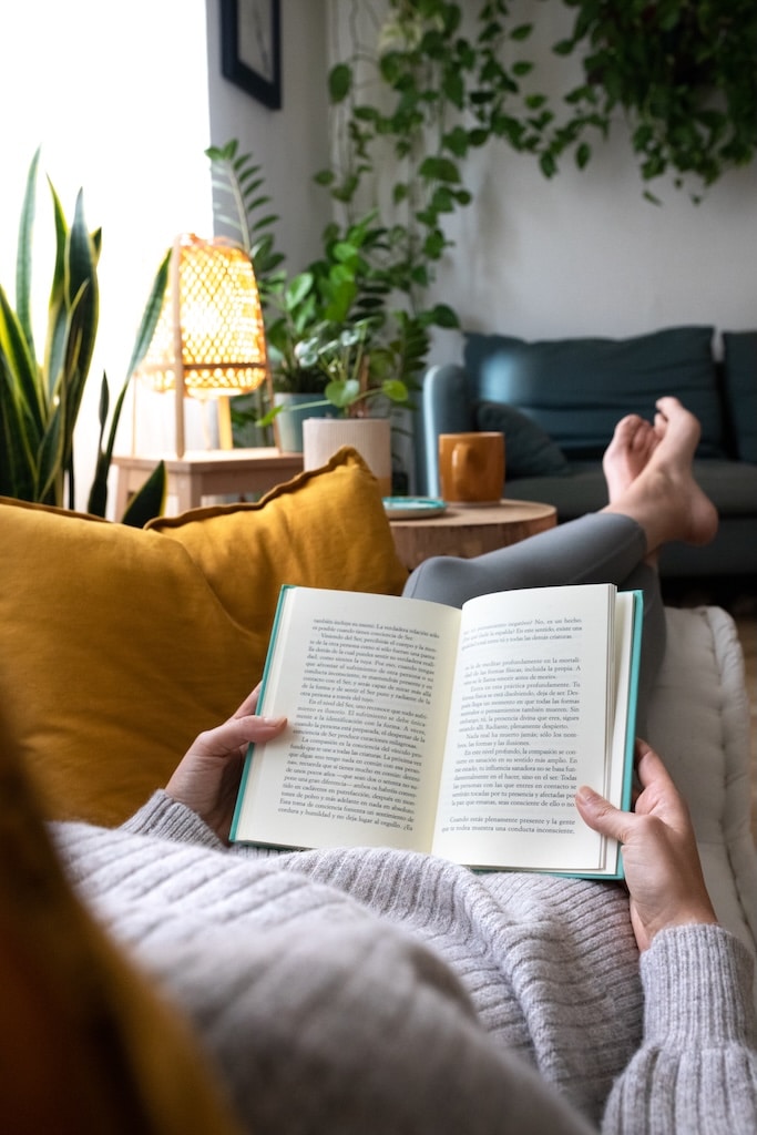 POV of young woman reading a book at home lying on couch.