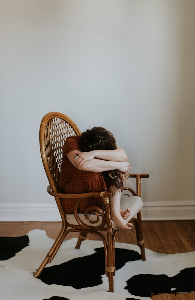 Impaired, upset woman sitting in wicker chair with her head down.