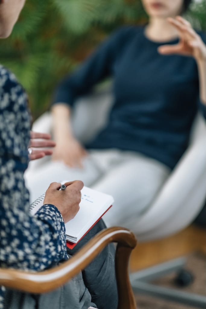 Mental health professional taking notes during therapy session with client.