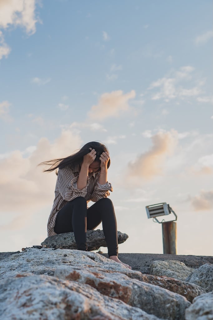 Young woman sitting on the beach with head in her hands.